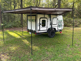 Explore nature! This small white camping trailer with an extended awning offers comfortable RV rental for outdoor travel in the woods.