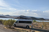 Enjoying a scenic lake view from an RV rental parked at a campsite, featuring a pop-top RV with mountains in the distance.