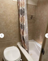 RV rental's compact bathroom: shower/tub combo, toilet, patterned curtain.