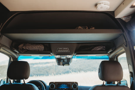 RV rental interior: view of front cabin, overhead storage with gear, and a control panel for lights. Prepared for travel.