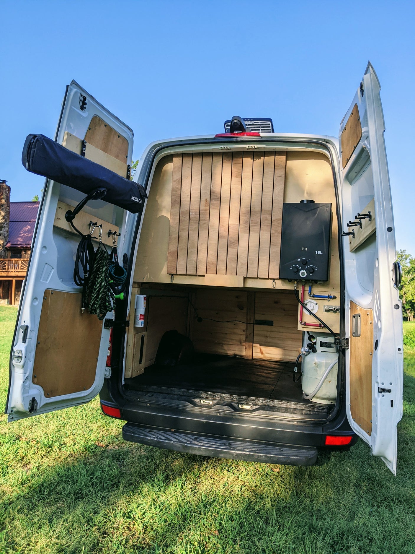 Rear view of an RV rental: a white camper van with open doors, revealing custom interior with water heater, shower, and storage.