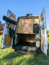 Rear view of an RV rental: a white camper van with open doors, revealing custom interior with water heater, shower, and storage.