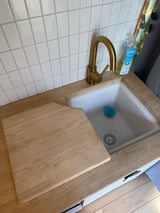 Compact rv rental kitchen featuring a white tiled backsplash, gold faucet, wooden countertop, and cutting board over the sink.