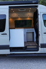 Spacious RV rental camper van interior with door open, revealing a bright kitchen, fridge, wood accents, and sleek storage.
