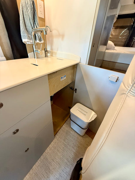 Modern rv rental kitchen featuring a compact sink, faucet, storage drawers, and a convenient pull-out trash can.