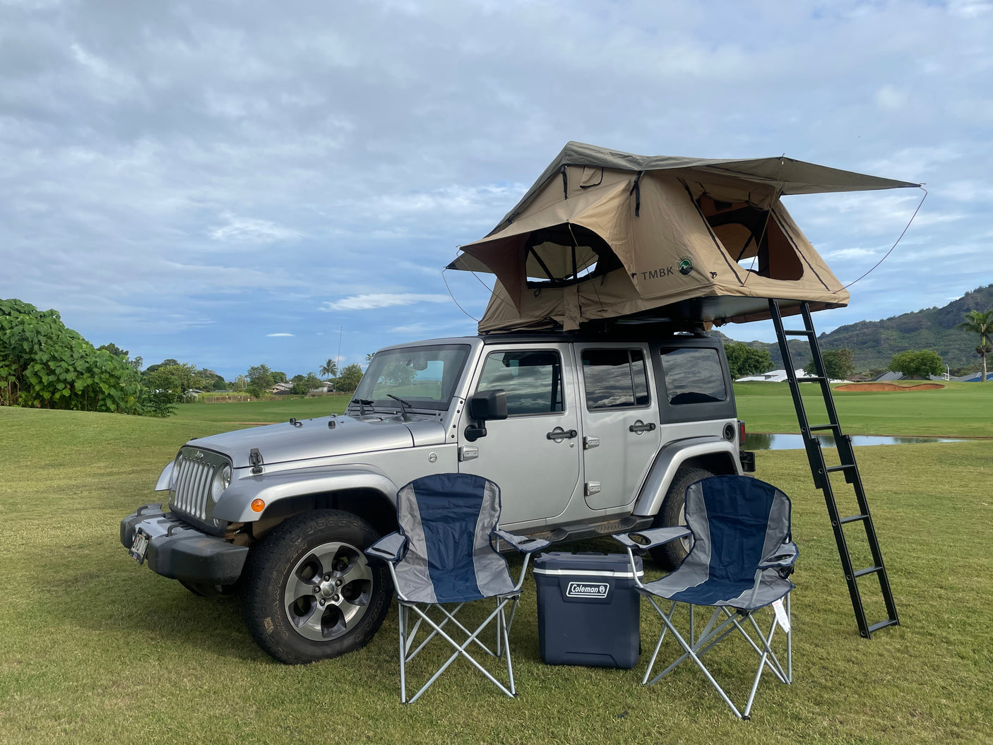 Silver Jeep Wrangler with rooftop tent, chairs, and cooler on a golf course. Great for an RV rental outdoor adventure.