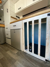Compact RV rental interior featuring a built-in dog crate, kitchen area with fridge, and storage. Perfect for pet travel.