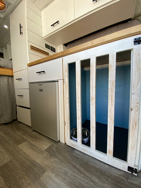 Compact RV rental interior featuring a built-in dog crate, kitchen area with fridge, and storage. Perfect for pet travel.