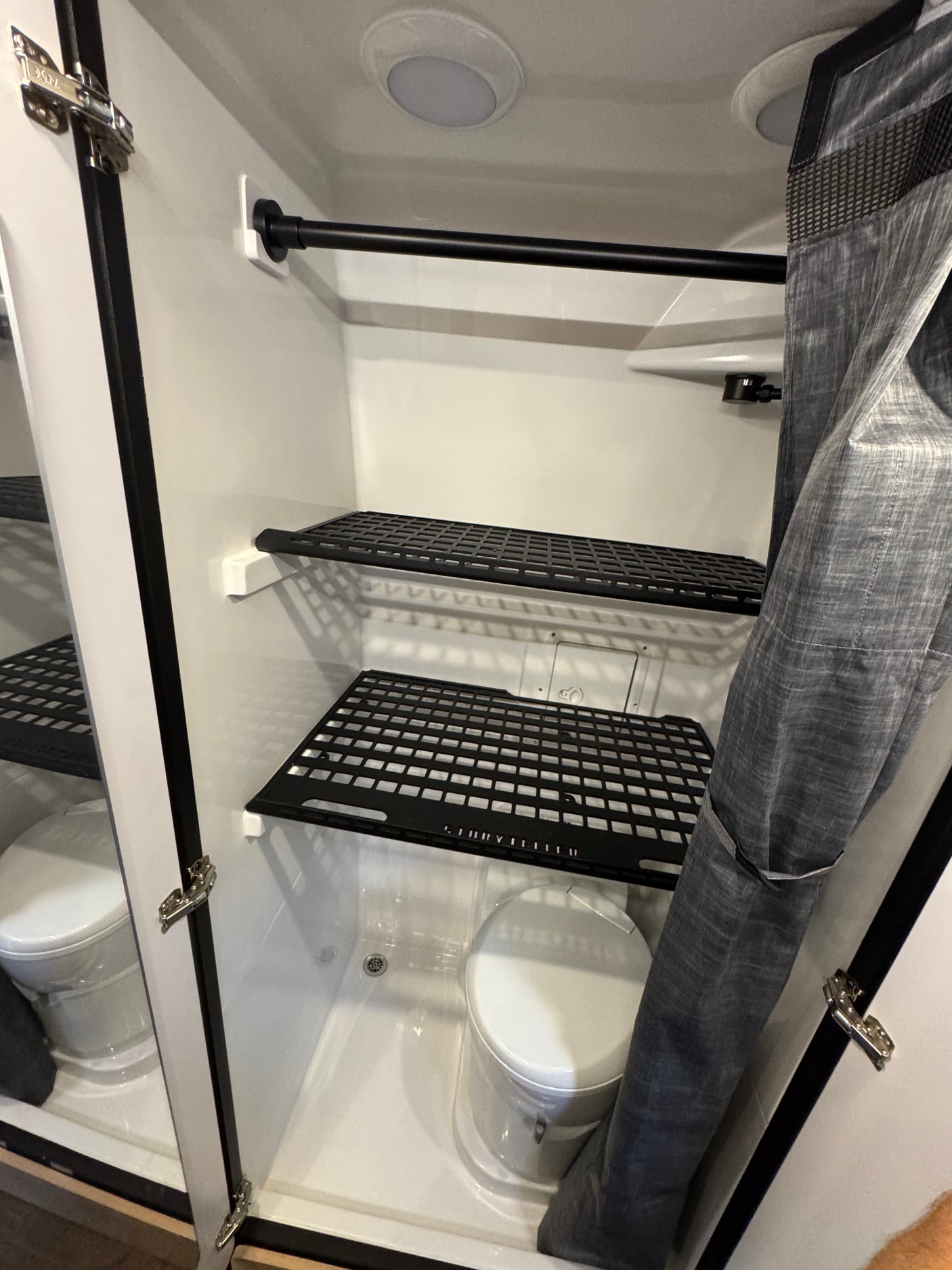 Compact RV rental wet bath featuring a toilet, shower area, storage shelves, and a privacy curtain.