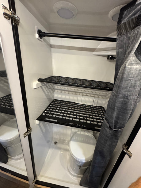 Compact RV rental wet bath featuring a toilet, shower area, storage shelves, and a privacy curtain.