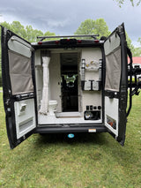 Open rear doors of an RV rental, revealing a compact interior with a toilet and organized storage for camping gear.