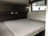 This RV rental features a cozy sleeping area with gray cushions, overhead storage, outlets, and a window.
