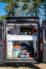 This RV rental offers comfort & utility: a camper van's interior with a cozy bed and smart storage for your adventures.