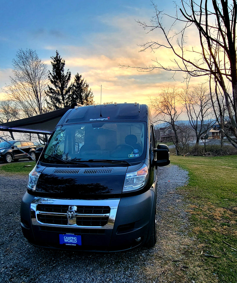 This black camper van RV rental sits on a gravel lot under a vibrant sunset sky, ready for your next trip. — photo 9
