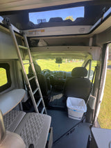 Inside an rv rental, this camper van features a ladder to a pop-top bed, front seats, and spacious mobile living.