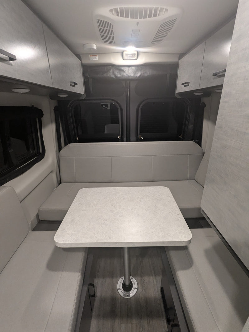 Inside this rv rental, a light grey dinette area with a central table is flanked by bench seating. Overhead cabinets line the walls. — photo 3