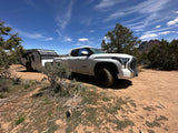 White pickup truck with an RV rental trailer, ready for overlanding adventures in a scenic desert mountain landscape.