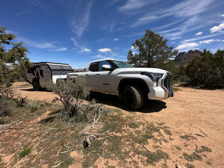 White pickup truck with an RV rental trailer, ready for overlanding adventures in a scenic desert mountain landscape.