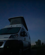 White pop-top camper van under a deep blue dusk sky. Your ultimate RV rental adventure awaits!