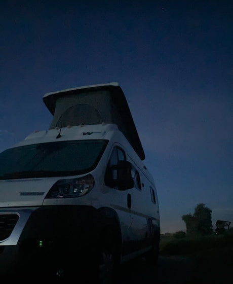 White pop-top camper van under a deep blue dusk sky. Your ultimate RV rental adventure awaits!