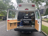 An RV rental's rear setup with open doors showing a handy collapsible table, water, and cooler storage for trips.