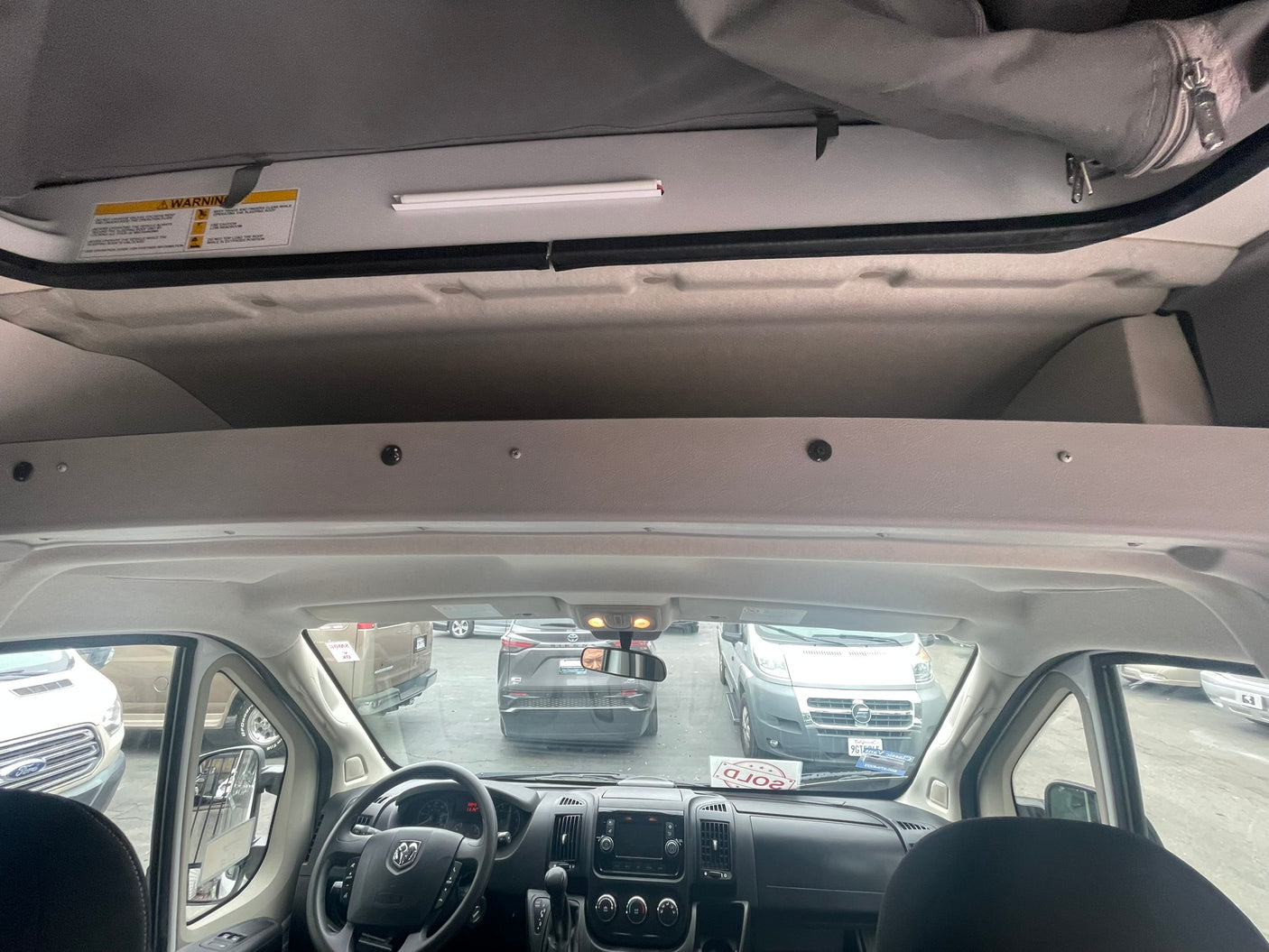RV rental camper van interior: driver's cockpit, dash, and overhead pop-top sleeping area with warning label.