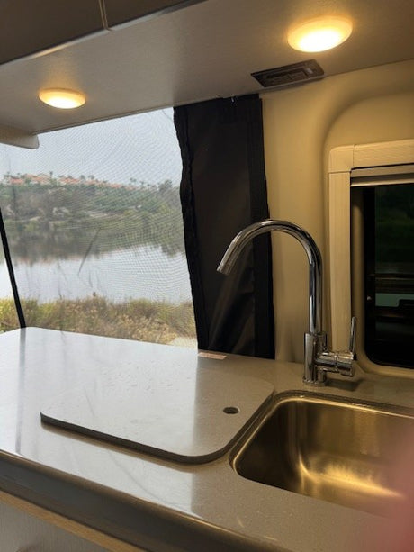 RV rental galley features a modern sink, spacious counter, and a stunning view of water and distant hills through the window.
