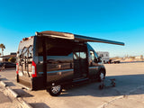 Grey camper van with extended awning, bike rack, and scooter. Perfect for an RV rental beach adventure under a clear sky.