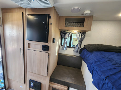 RV rental interior: cozy bed, fridge, TV, & dinette area in light wood finishes.