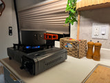 Cooking in an RV rental! A portable gas stove with a pot, next to a woven basket and salt/pepper grinders on the counter.