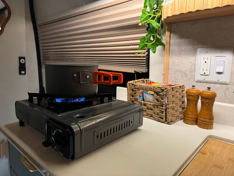 Cooking in an RV rental! A portable gas stove with a pot, next to a woven basket and salt/pepper grinders on the counter.