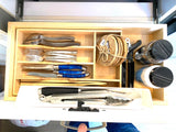 Compact rv rental kitchen drawer: organized silverware, blue-handled knives, tongs, and spice jars neatly stored.