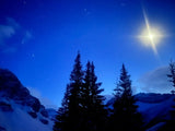 Perfect for an RV rental trip: A serene winter night with stars, moon, snowy mountains, & dark evergreen trees.