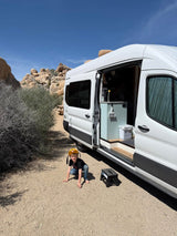 White camper van RV rental set up in a sunny desert park, showing interior; child playing nearby.
