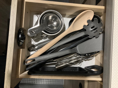 Organized kitchen utensils in an RV rental drawer, including measuring cups, a wooden spoon, and a whisk.