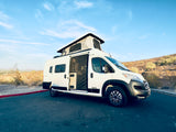 White pop-top camper van for RV rental, with open side door, parked in sunny desert landscape.