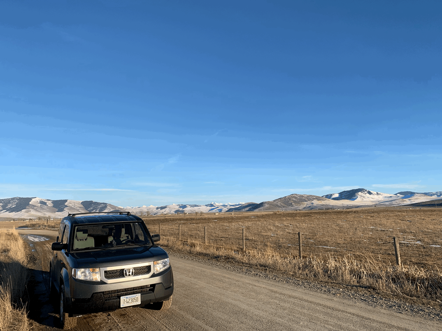 Honda Element on a Montana dirt road with snowy mountains. Experience similar vast landscapes with an RV rental.