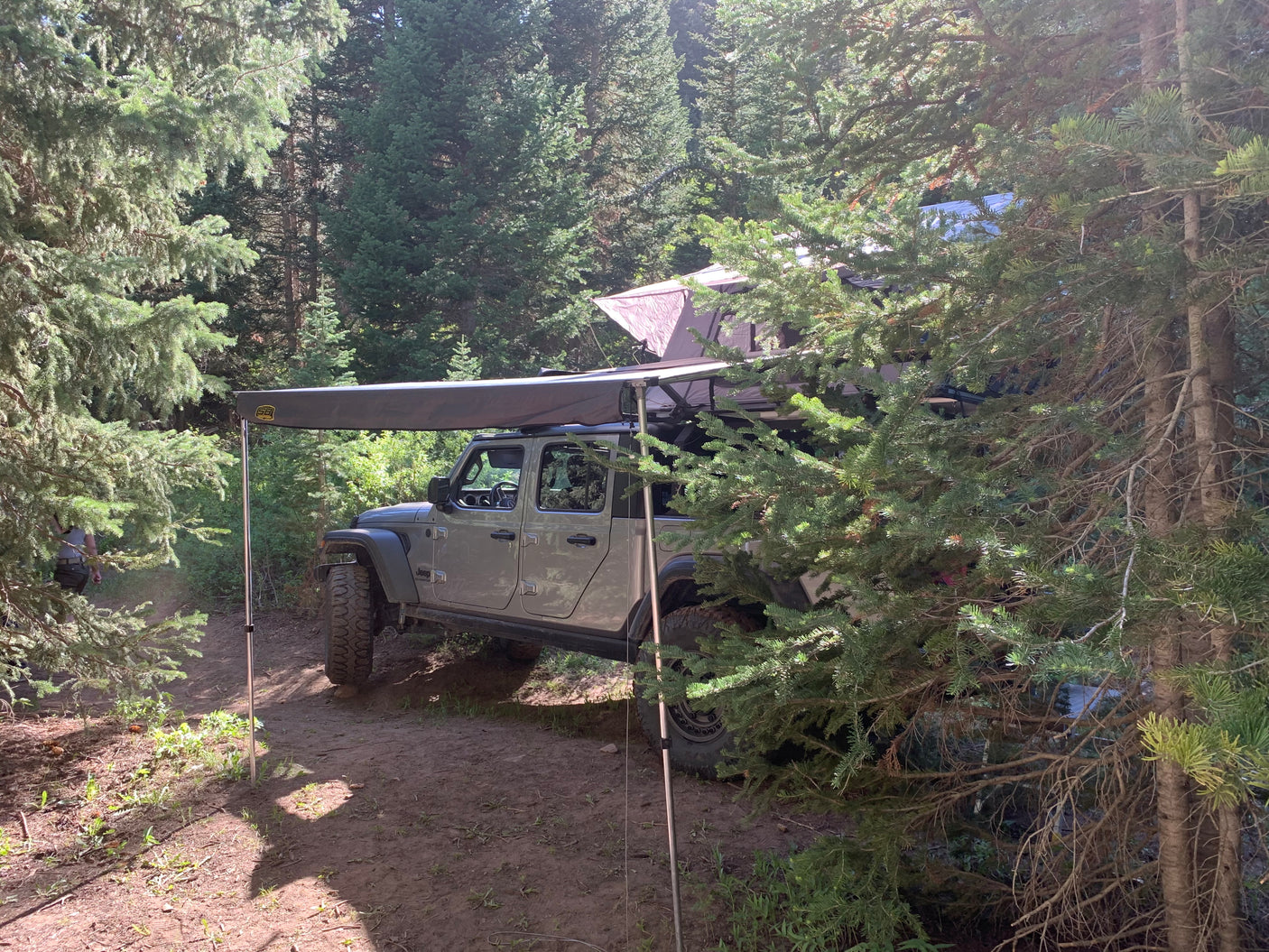 RV rental: Jeep Gladiator with roof tent & awning parked in a forest campsite, ready for adventure.