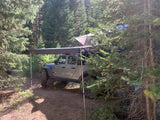 RV rental: Jeep Gladiator with roof tent & awning parked in a forest campsite, ready for adventure.