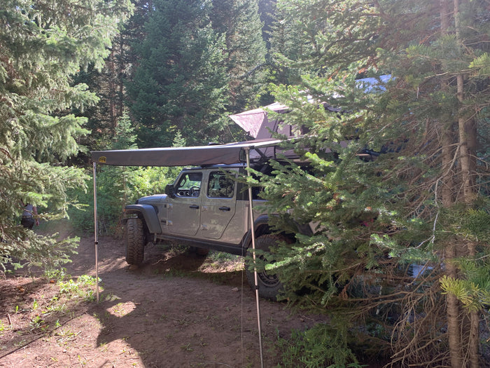 RV rental: Jeep Gladiator with roof tent & awning parked in a forest campsite, ready for adventure.