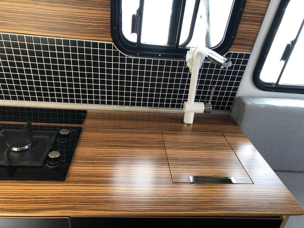 RV rental kitchen: stylish wood-grain counter, black/white tiled backsplash, gas cooktop, and covered sink. — photo 17