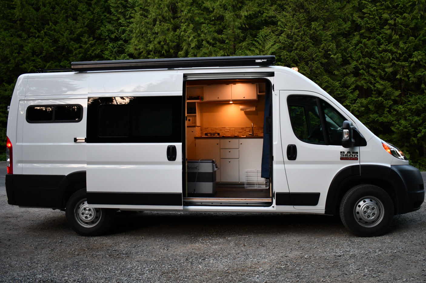 White Ram ProMaster camper van, side door open to illuminated kitchen interior. Explore with this RV rental.
