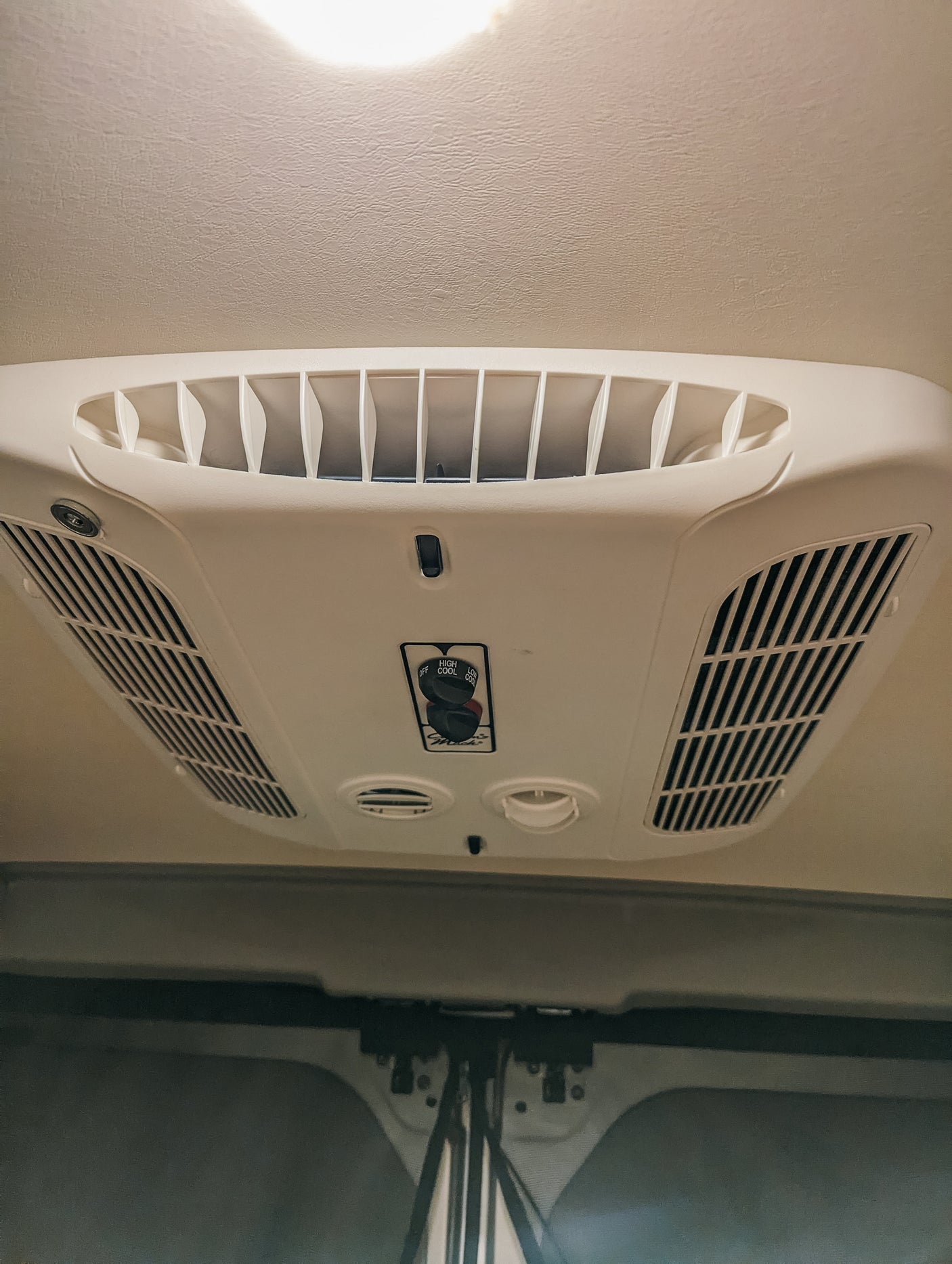 White overhead RV rental AC unit with vents & control knobs for fan/cool. Essential for comfortable travel.