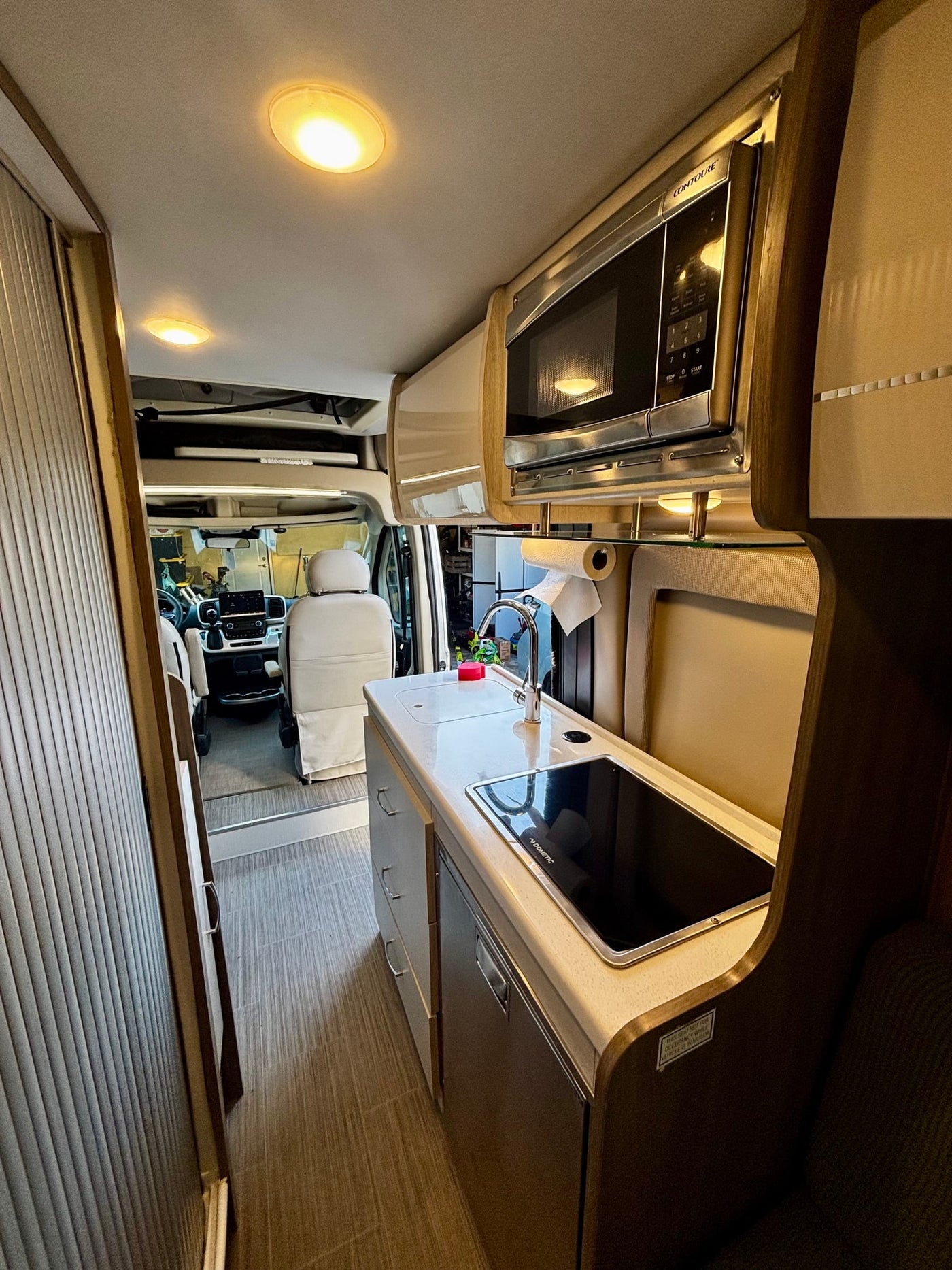 Bright rv rental kitchen: Dometic cooktop, sink, and Contoure microwave visible. Spacious interior with driver's cabin. — photo 18