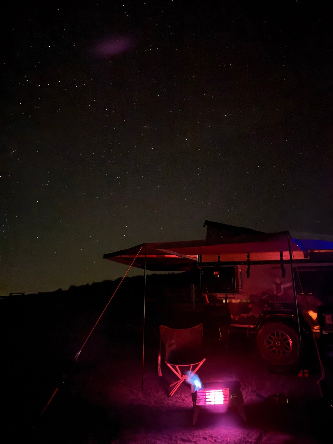Experience starry nights! An rv rental with awning, chair, and glowing heater illuminates a cozy camp under a beautiful night sky. — photo 20