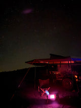 Experience starry nights! An rv rental with awning, chair, and glowing heater illuminates a cozy camp under a beautiful night sky.