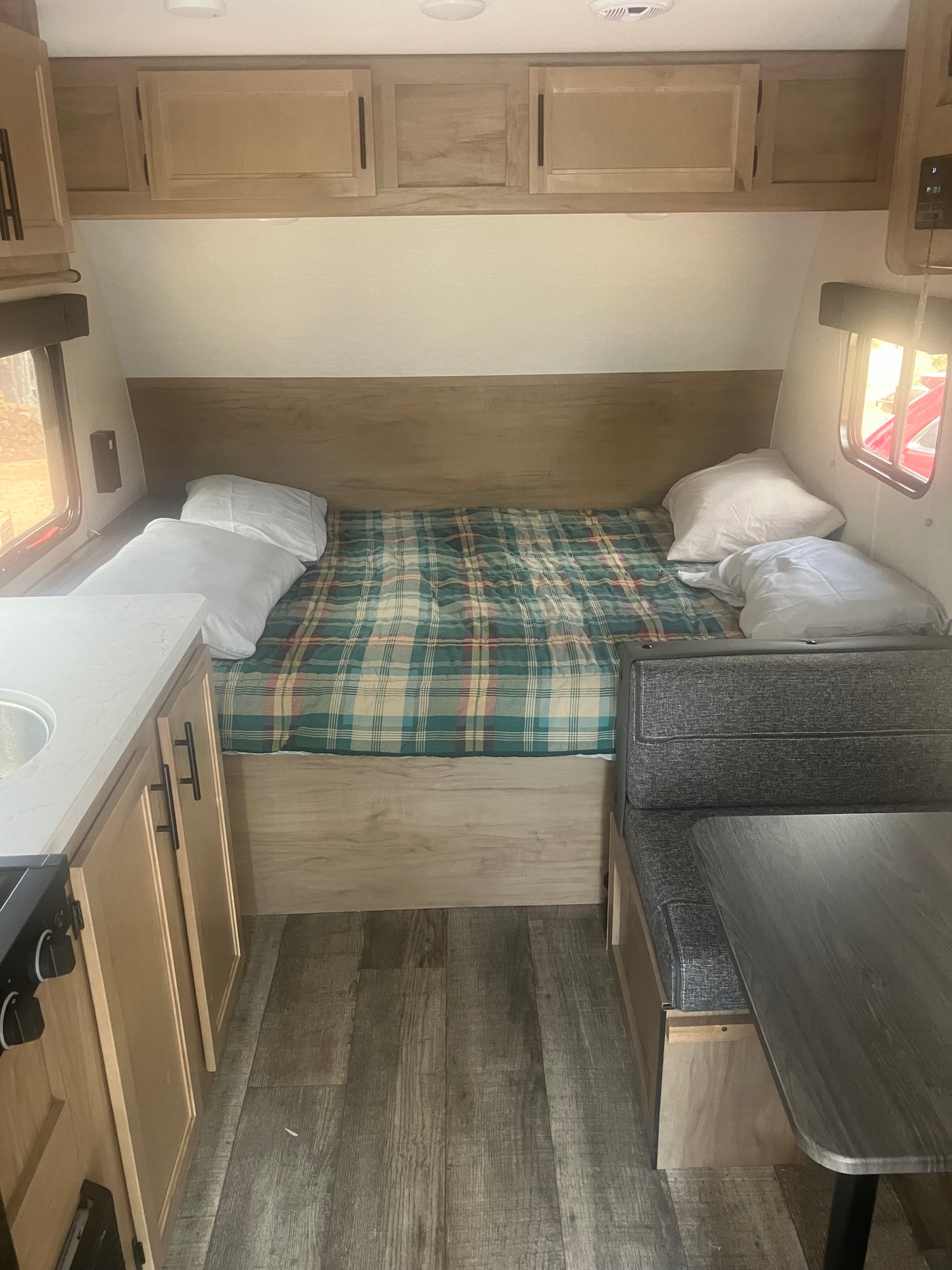 Compact RV rental interior featuring a cozy bed, kitchen area with sink, and a dinette with table. — photo 6