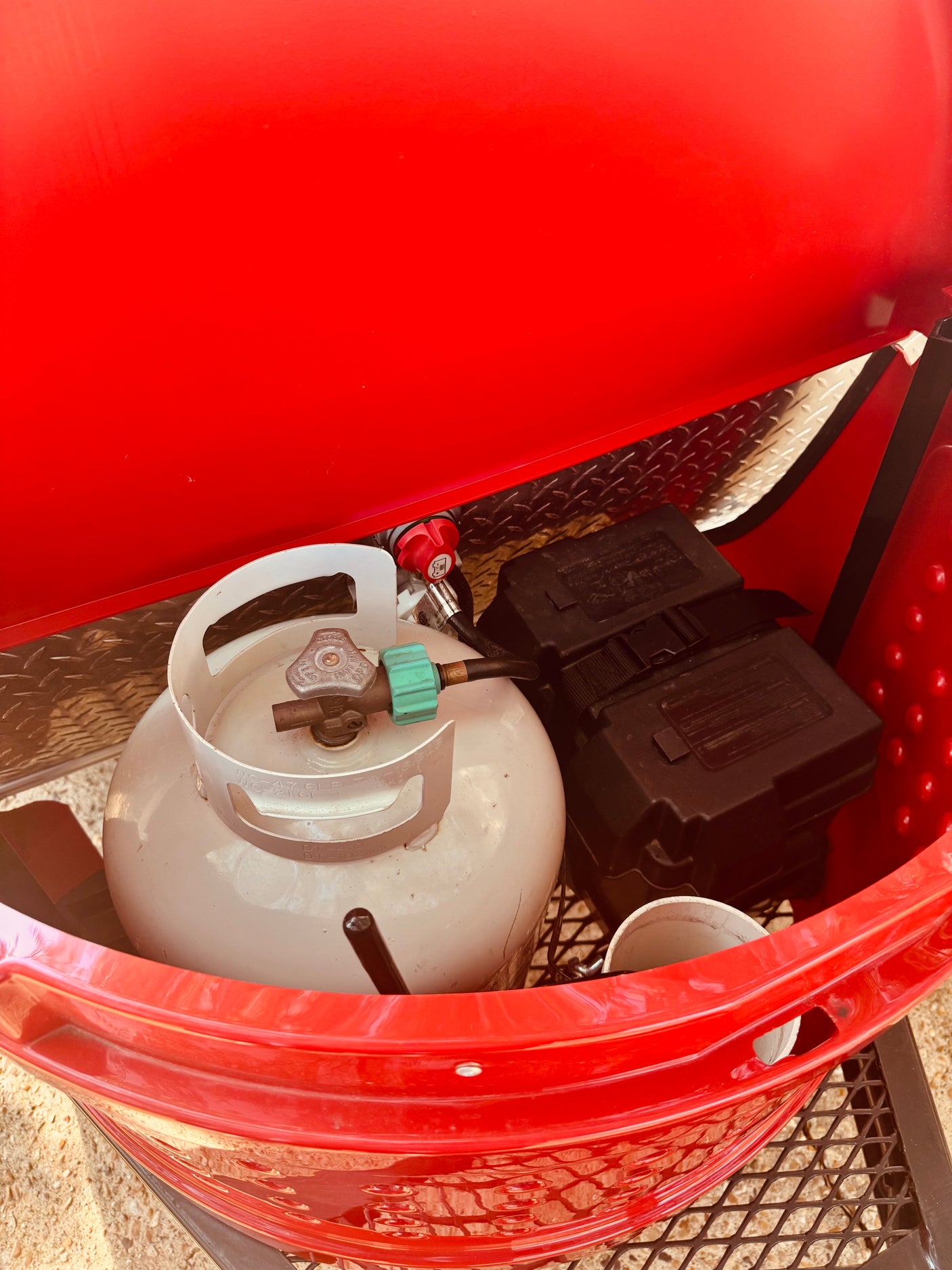 Propane tank, regulator, and battery box within an **rv rental**'s portable fire pit setup. Essential camping gear.