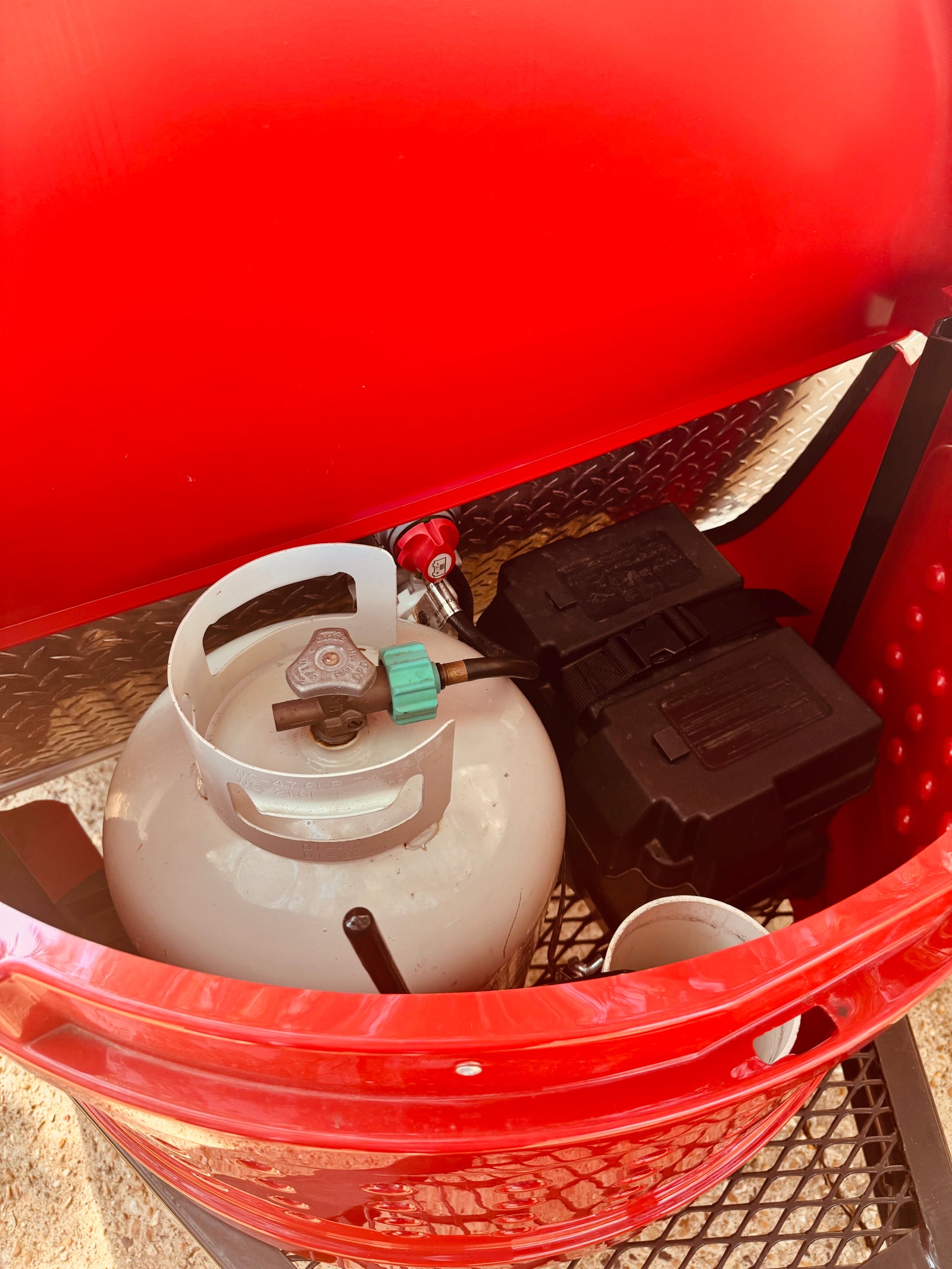 Propane tank, regulator, and battery box within an **rv rental**'s portable fire pit setup. Essential camping gear.