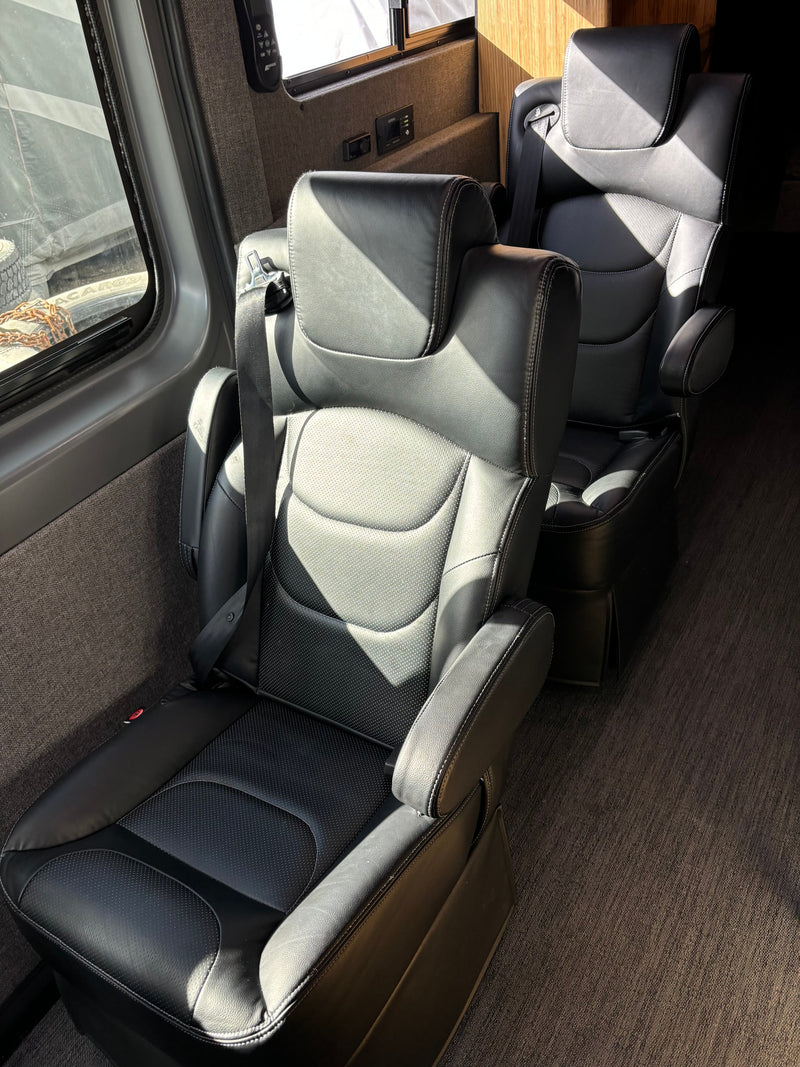 Sunlight bathes luxurious black leather captain's chairs with seatbelts in this RV interior, perfect for rv rental. — photo 9